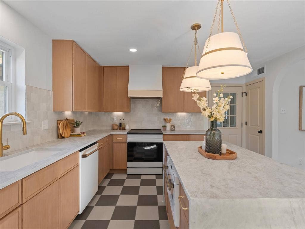 Kitchen featuring light wood-finish cabinetry, a central island with a stone countertop, a brass faucet, a custom range hood, and a checkerboard pattern tile floor