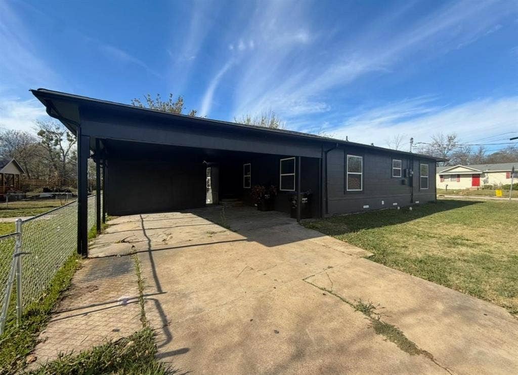 3901 Park Street, Greenville, TX 75401 Single-story exterior featuring a dark-toned facade, an integrated carport, a concrete driveway, and a chain-link perimeter fence