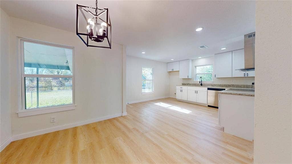 3901 Park Street, Greenville, TX 75401 Open-concept area featuring wood-finish flooring, white cabinetry, stone-finish countertops, stainless steel appliances, and a geometric metal pendant light