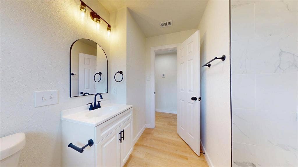 3901 Park Street, Greenville, TX 75401 Bathroom featuring a vanity with a white cabinetry base, arched wall mirror, stone-finish shower surround, and matte black fixtures