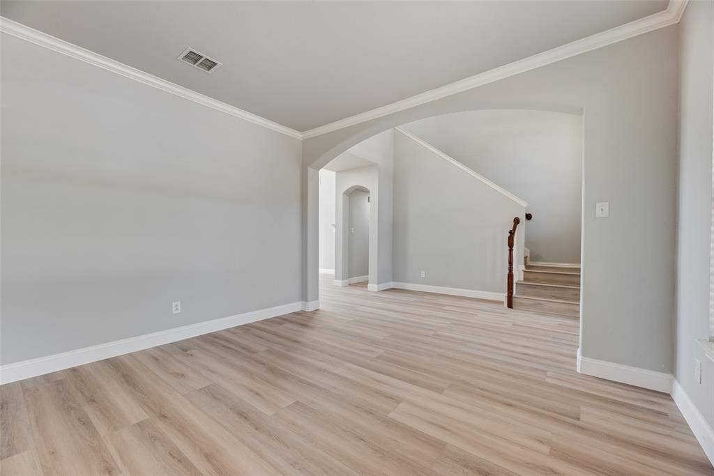 1716 Clarke Springs Drive, Allen, TX 75002 Interior space featuring wood-finish flooring, neutral wall tones, arched wall openings, crown molding, and a staircase with a dark wood handrail