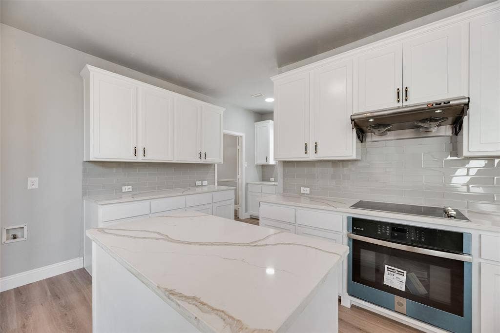 1716 Clarke Springs Drive, Allen, TX 75002 Kitchen featuring a central island with a quartz countertop, white shaker-style cabinetry, a light gray subway tile backsplash, and stainless steel appliances
