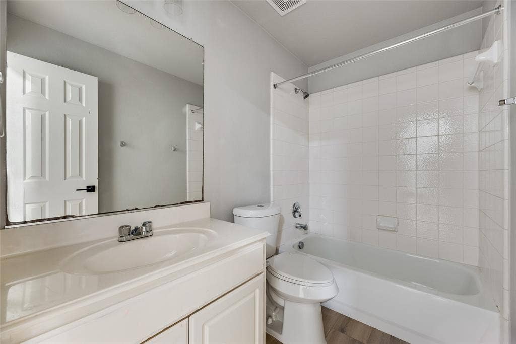 1716 Clarke Springs Drive, Allen, TX 75002 Bathroom featuring a white vanity cabinet with an integrated sink, a large wall-mounted mirror, a two-piece toilet, and a tub-shower combination with white wall tile