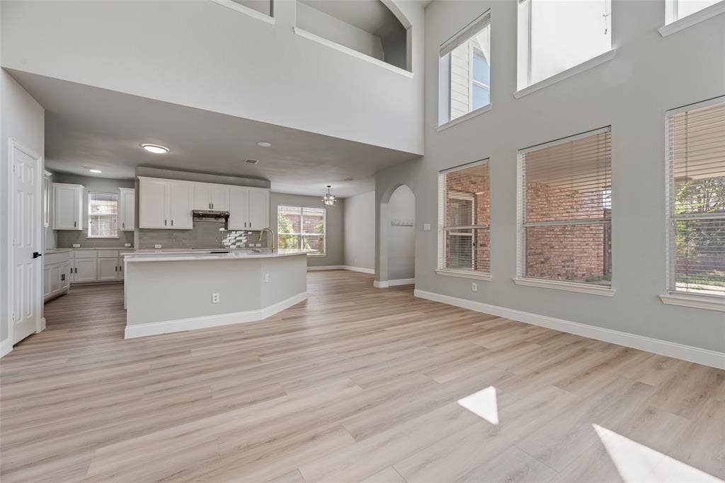 1716 Clarke Springs Drive, Allen, TX 75002 Two-story height ceiling with multi-level windows, wood-finish flooring, kitchen featuring white cabinetry and a center island, and arched architectural details
