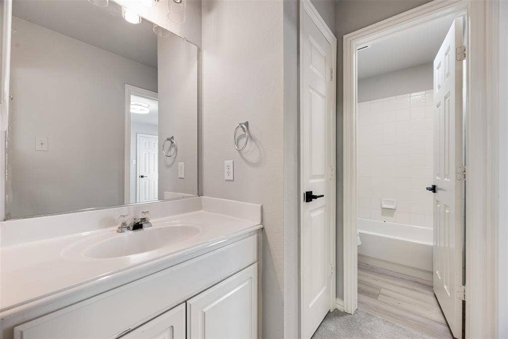 1716 Clarke Springs Drive, Allen, TX 75002 Bathroom featuring a white vanity cabinet with an integrated sink, a large wall-mounted mirror, brushed metal fixtures, and a shower-tub combination with tile surround