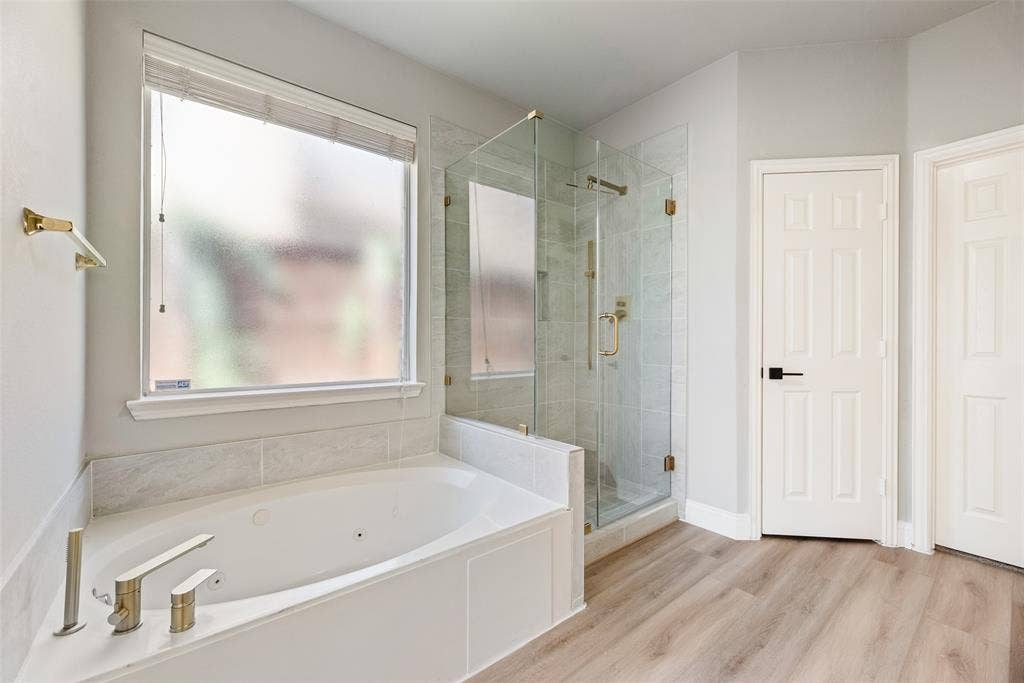 1716 Clarke Springs Drive, Allen, TX 75002 Jetted soaking tub with deck-mounted metallic faucet, glass-enclosed walk-in shower with tiled surround, wood-finish flooring, and frosted window