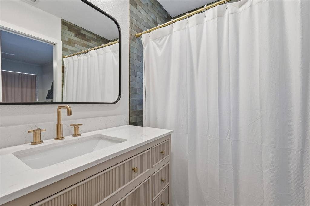 2810 Bonnie View Road, Dallas, TX 75216 Bathroom vanity featuring a fluted cabinet base, stone-surface countertop, rectangular undermount sink, brass-finish widespread faucet, and a black-framed rectangular wall mirror