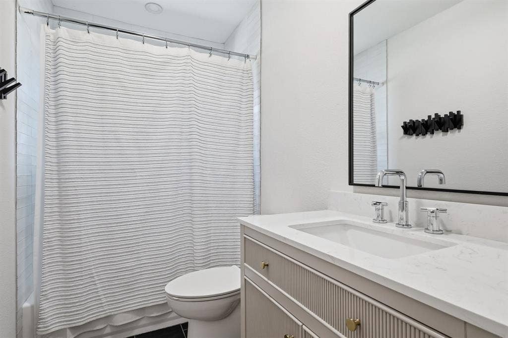 2810 Bonnie View Road, Dallas, TX 75216 Bathroom featuring a vanity with fluted cabinetry, light-toned countertop, integrated rectangular sink, polished chrome widespread faucet, and a rectangular mirror with a black frame