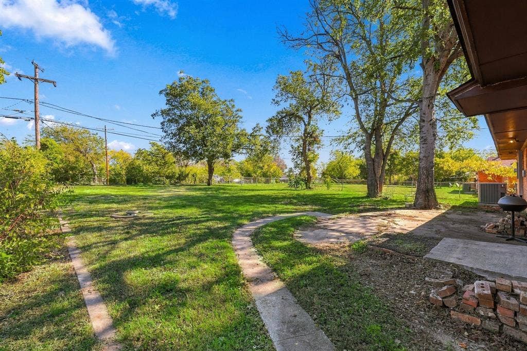 2810 Bonnie View Road, Dallas, TX 75216 Expansive backyard featuring a concrete patio, stone pathway, mature trees, and perimeter chain-link fencing