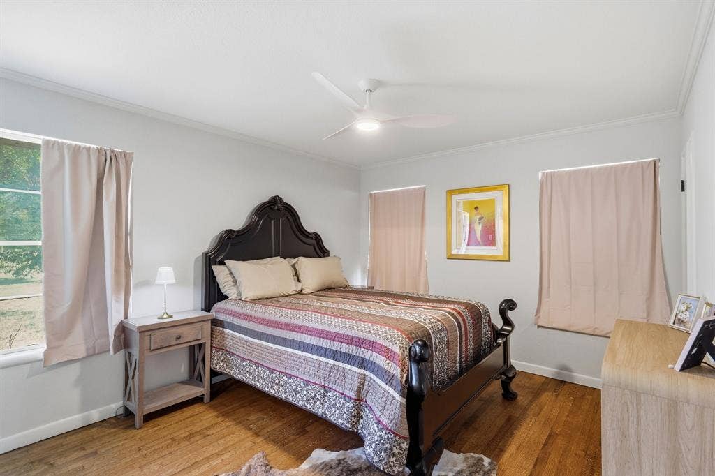 2810 Bonnie View Road, Dallas, TX 75216 Bedroom featuring wood-finish flooring, three windows with natural light, and a white ceiling fan with integrated lighting