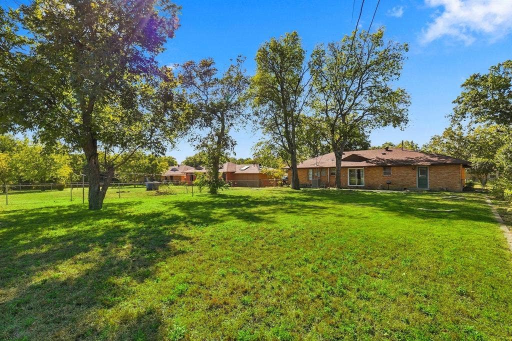 2810 Bonnie View Road, Dallas, TX 75216 Expansive backyard featuring a brick exterior residence, mature shade trees, and a perimeter fence