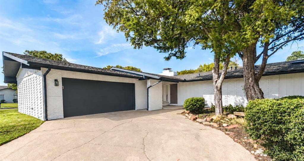 13936 Tanglewood Place, Farmers Branch, TX 75234 This Mid-century modern home, built in1960, features white painted brick masonry, vertical wood-panel siding, attached two-car garage, and low-pitch roofline