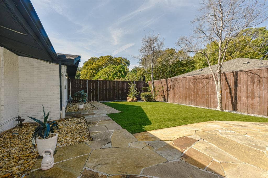13936 Tanglewood Place, Farmers Branch, TX 75234 Private backyard featuring expansive flagstone patio, synthetic turf lawn, white painted brick exterior, and perimeter wood privacy fencing