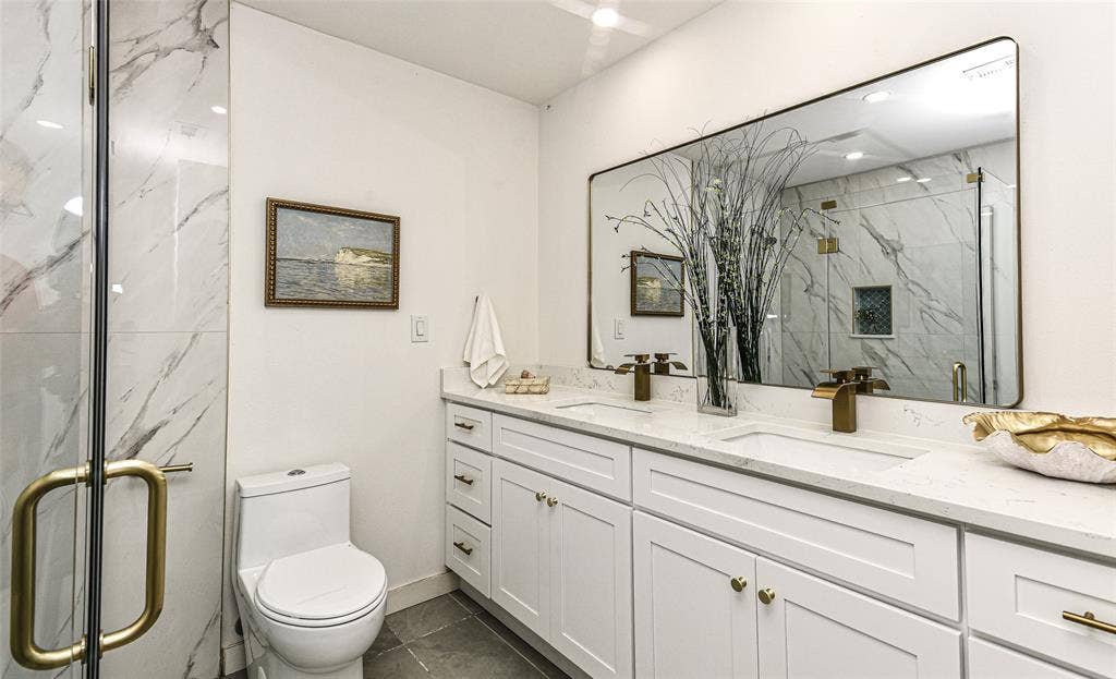 13936 Tanglewood Place, Farmers Branch, TX 75234 Your Guests will love the Dual-sink vanity with white shaker-style cabinetry, quartz countertop, and brass fixtures, accompanied by a large wall-to-wall mirror and a walk-in shower