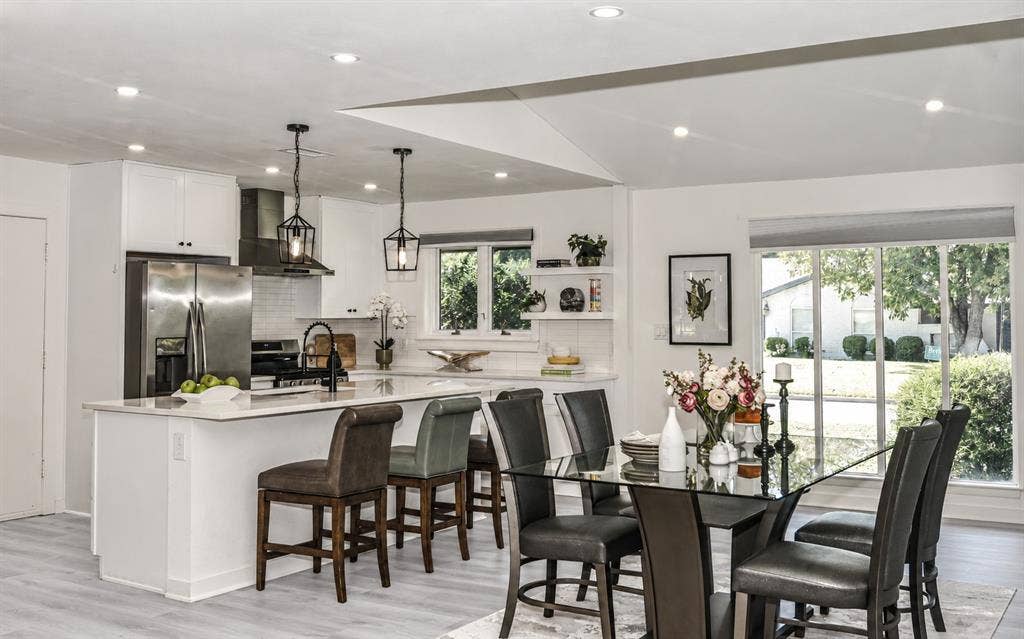 13936 Tanglewood Place, Farmers Branch, TX 75234 Open-concept kitchen featuring a waterfall-edge stone island, stainless steel appliances, matte black fixtures, recessed lighting, and white cabinetry