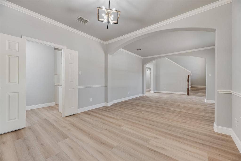 1716 Clarke Springs Drive, Allen, TX 75002 Open interior featuring wood-finish flooring, architectural arched openings, crown molding, chair rail trim, and a modern geometric light fixture