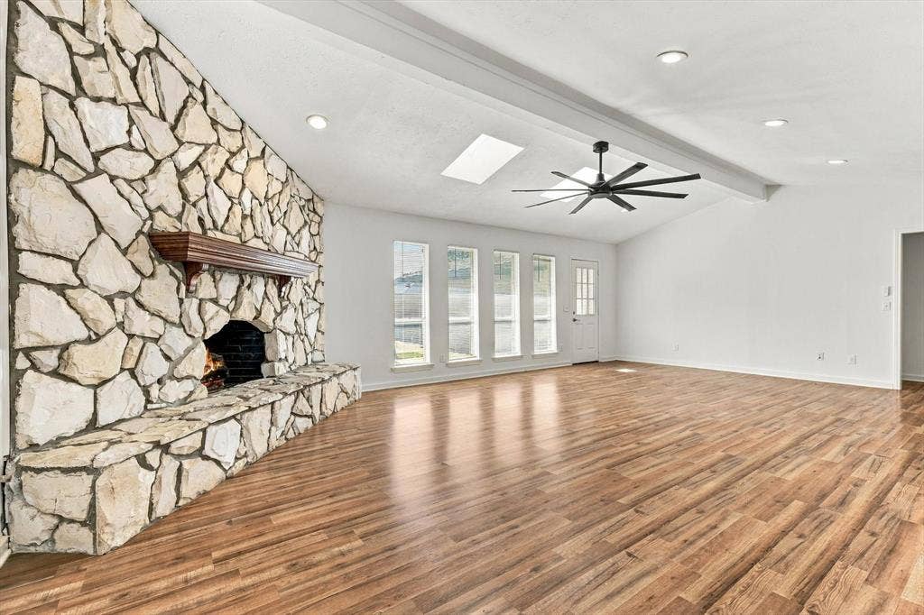 1900 Ports O Call Drive, Plano, TX 75075 Floor-to-ceiling stone fireplace with a wood mantel, wood-finish flooring, vaulted ceiling with recessed lighting, skylights, and a multi-blade ceiling fan