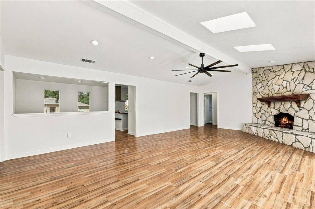 1900 Ports O Call Drive, Plano, TX 75075 Living area featuring wood-finish flooring, floor-to-ceiling natural stone fireplace, skylights, recessed lighting, and a modern ceiling fan