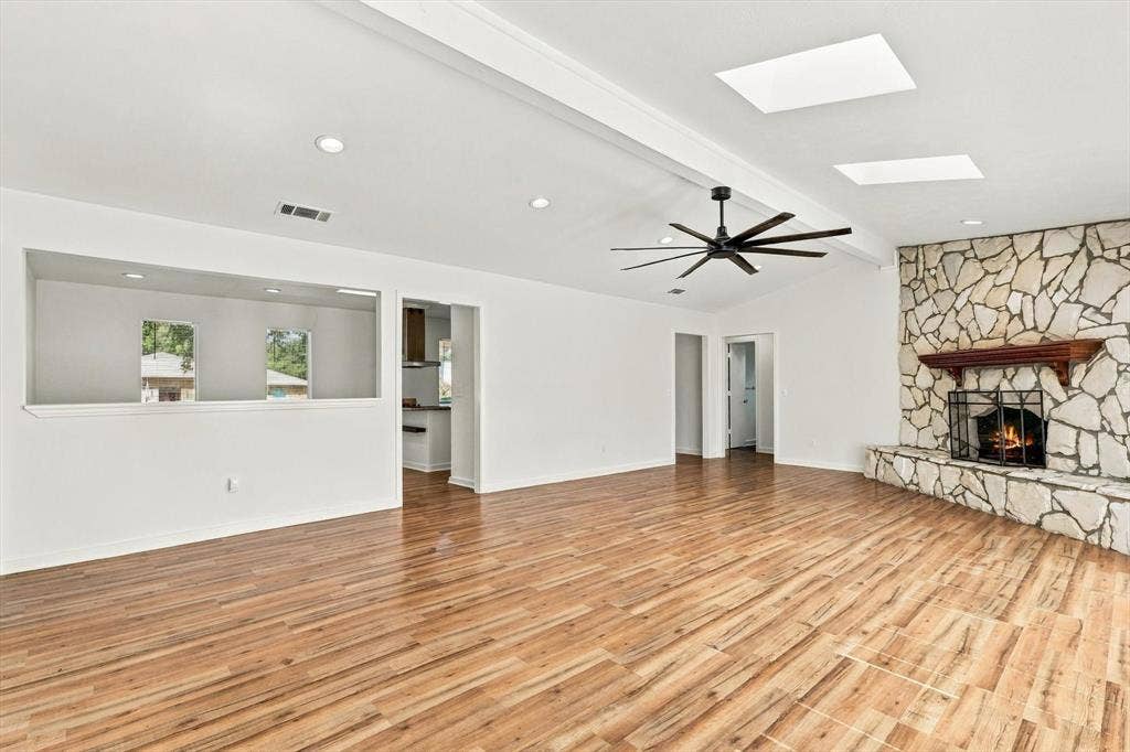 1900 Ports O Call Drive, Plano, TX 75075 Open-concept interior featuring wood-finish flooring, a full-height stone fireplace with a wooden mantel, multiple skylights, and a multi-blade ceiling fan