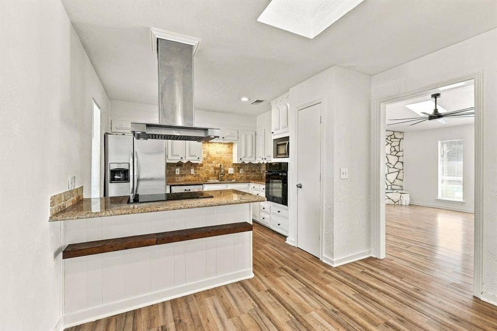 1900 Ports O Call Drive, Plano, TX 75075 Kitchen featuring stone countertops, white cabinetry, stainless steel vent hood, wood-finish flooring, and a skylight
