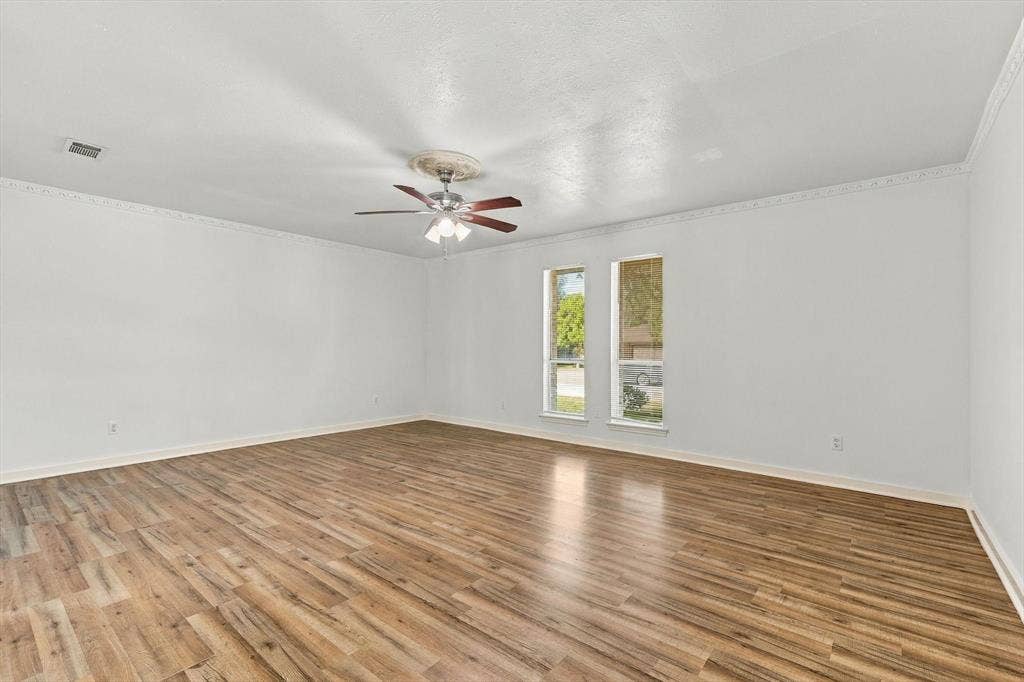 1900 Ports O Call Drive, Plano, TX 75075 Spacious room featuring wood-finish flooring, crown molding, dual windows, and a central ceiling fan with integrated light fixture