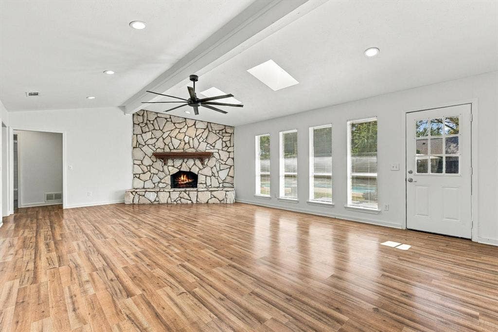 1900 Ports O Call Drive, Plano, TX 75075 Spacious room featuring wood-finish flooring, a floor-to-ceiling stone fireplace, skylights, recessed lighting, and a multi-blade ceiling fan