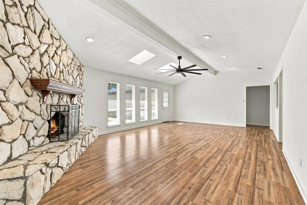 1900 Ports O Call Drive, Plano, TX 75075 Full-height floor-to-ceiling stone fireplace with a prominent wooden mantel, wood-finish flooring, recessed lighting, dual skylights, and a ceiling fan