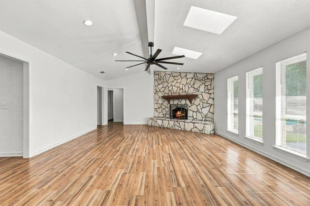 1900 Ports O Call Drive, Plano, TX 75075 Vaulted ceiling with skylights, wood-finish flooring, full-height stone-clad fireplace, and large multi-pane windows