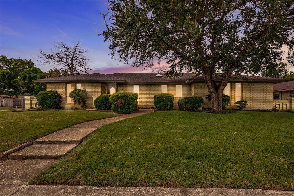 1900 Ports O Call Drive, Plano, TX 75075 Single-story brick exterior featuring a low-pitch roofline, vertical window accents, concrete walkway, and mature landscaping