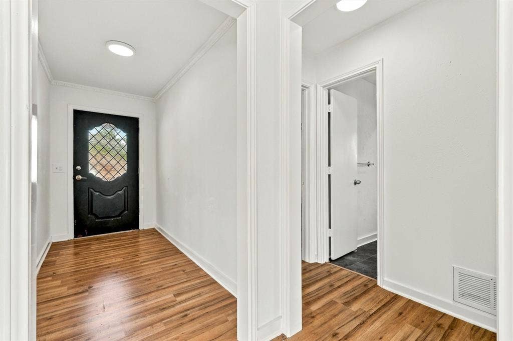 1900 Ports O Call Drive, Plano, TX 75075 Entryway featuring wood-finish flooring, white walls, crown molding, and a solid black exterior door with decorative lattice-patterned glass