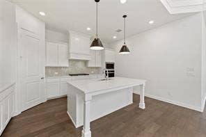 15638 Kestrel Mews, Frisco, TX 75035 Kitchen featuring white shaker-style cabinetry, quartz countertops, a central island with a built-in sink, stainless steel dual wall ovens, and wood-finish flooring