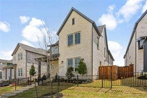 15638 Kestrel Mews, Frisco, TX 75035 Two-story masonry exterior featuring light-toned brick cladding, multi-pane windows, a steep roofline, and a black metal perimeter fence