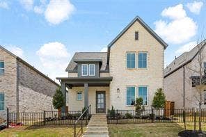 15638 Kestrel Mews, Frisco, TX 75035 Two-story exterior featuring light-toned brick masonry, a covered front porch with dark structural columns, multi-pane windows, and a metal perimeter fence