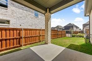 15638 Kestrel Mews, Frisco, TX 75035 Covered concrete patio featuring a masonry-clad support pillar, wooden privacy fencing, and a sodded lawn