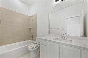 15638 Kestrel Mews, Frisco, TX 75035 Bathroom featuring a white vanity with a composite countertop, an integrated rectangular sink, a large wall-mounted mirror, and a tiled shower-tub surround with a built-in shelf