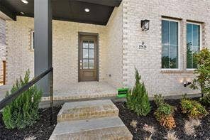 15638 Kestrel Mews, Frisco, TX 75035 Light-colored brick exterior featuring a recessed entry with a dark-finished ceiling, a multi-pane wood-frame entry door, and stone steps leading to the threshold