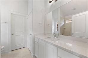 15638 Kestrel Mews, Frisco, TX 75035 Bathroom vanity featuring white cabinetry, a light-toned solid surface countertop, an integrated rectangular sink, a chrome faucet, and a large frameless wall mirror