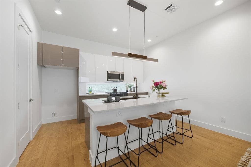 Kitchen featuring two-tone flat-panel cabinetry, quartz countertops, a geometric tile backsplash, stainless steel built-in microwave, and recessed lighting