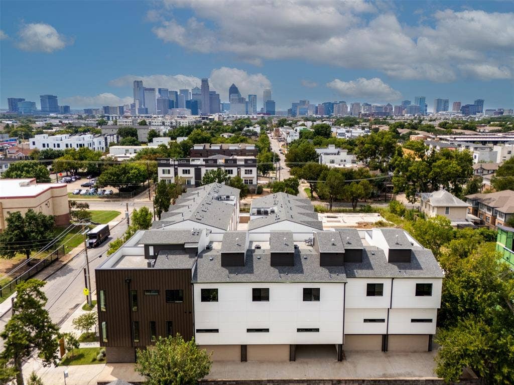 Contemporary multi-story townhome complex featuring metal and composite exterior siding, tiered rooflines, flat-roof terraces, and integrated ground-level garage bays