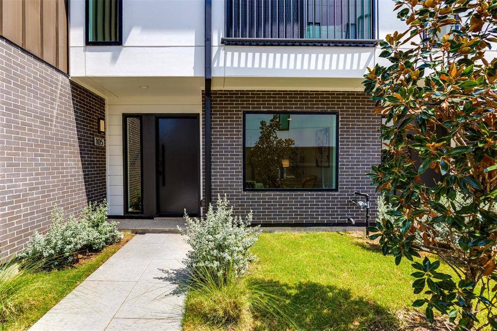 Modern exterior featuring charcoal brick veneer, crisp white horizontal siding, oversized picture window with black framing, and a paved stone walkway