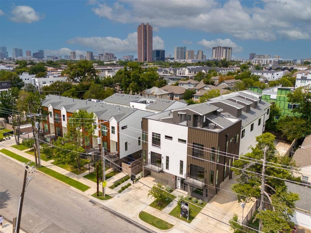 Multi-level townhome exterior featuring vertical metal siding, glass balcony railings, a concrete driveway, and a flat roofline