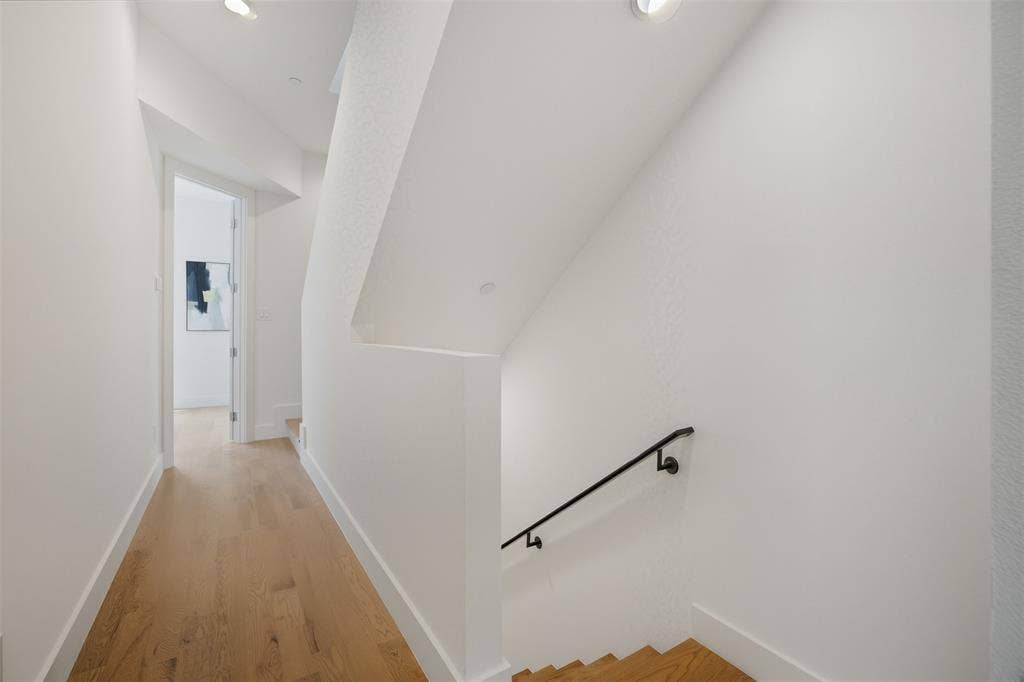 Staircase featuring wood-finish treads, matte black wall-mounted handrail, light wood-finish flooring, and recessed ceiling lighting