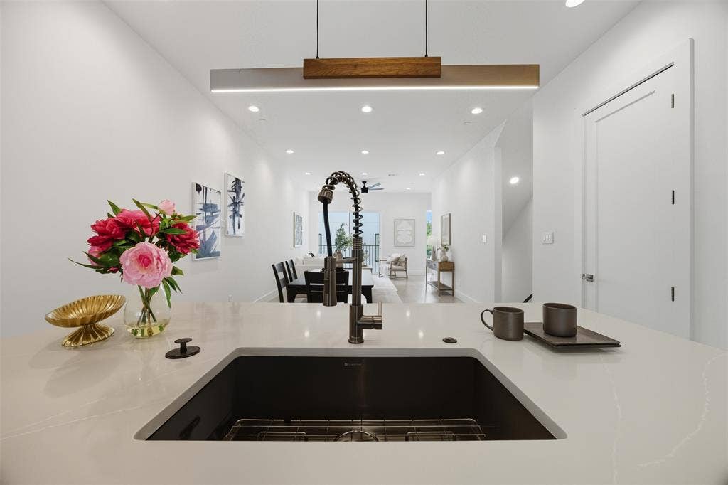 Quartz countertop, undermount sink with a high-arch pulldown faucet, and linear wood-accented pendant lighting