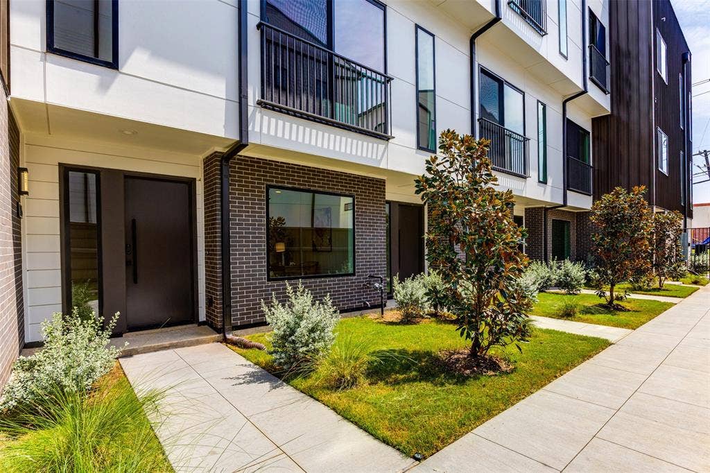 Modern multi-story exterior featuring dark brick masonry, white horizontal siding, metal balcony railings, and concrete walkways