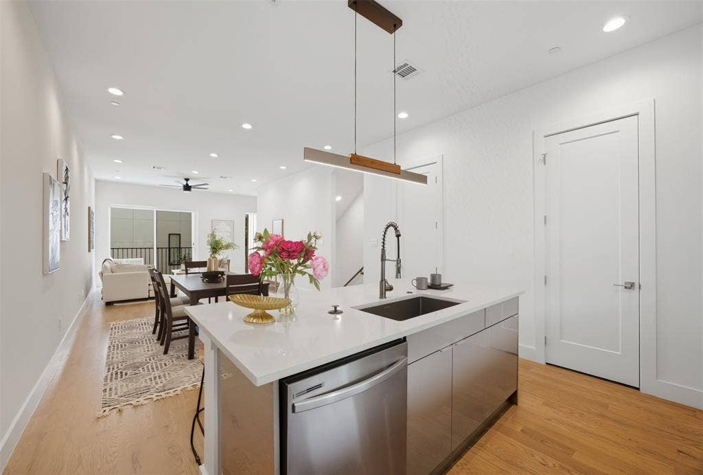 Kitchen island featuring a white stone countertop, undermount stainless steel sink, pull-down chrome faucet, and stainless steel dishwasher