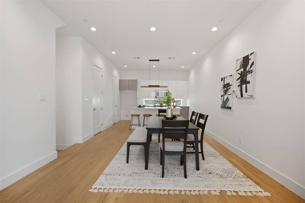 Open concept kitchen and dining area featuring wood-finish flooring, recessed lighting, white cabinetry, a center island with a stone-surface countertop, and a contemporary linear pendant light fixture