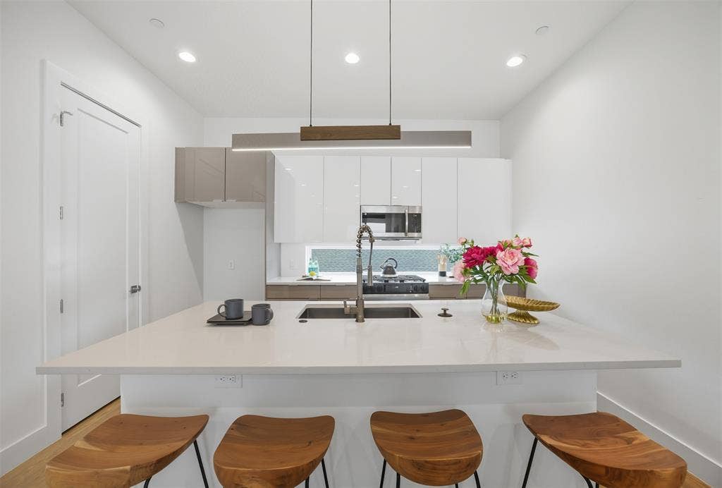 Kitchen featuring a central island with a solid-surface countertop, high-gloss flat-panel cabinetry, a stainless steel undermount sink with a gooseneck faucet, recessed ceiling lighting, and a linear pendant fixture