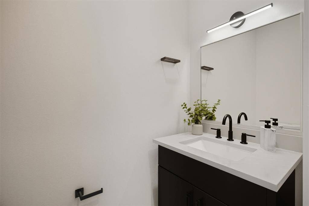 Dark vanity featuring a light-toned solid surface countertop with an integrated rectangular sink, matte black widespread faucet, framed wall-mounted mirror, and linear LED vanity light