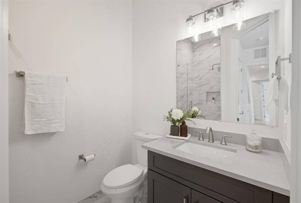 Bathroom featuring a dark wood-finish vanity, light-toned stone countertop, integrated rectangular sink, brushed-nickel faucet, and three-light wall-mounted fixture