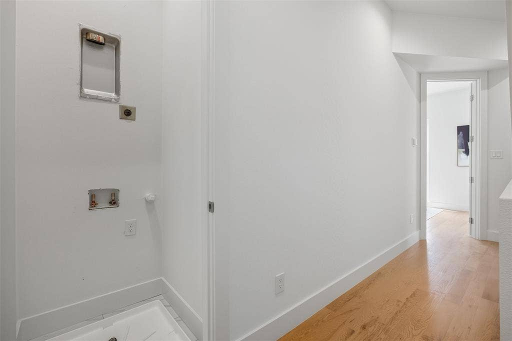 Utility area featuring wood-finish flooring, recessed dryer venting, dedicated water hookups, and a built-in drain pan